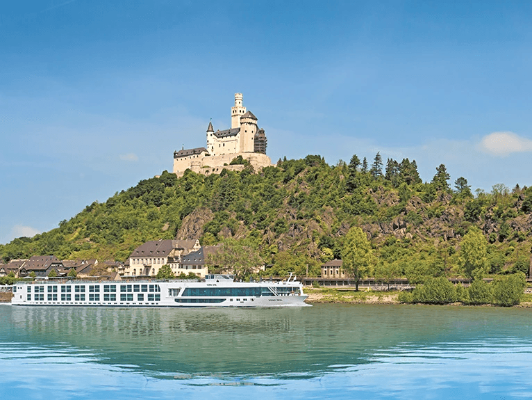 The Scenic Opal Space-Ship on the Rhine River, with the backdrop of towering mountains and the historic Marksburg Castle perched on top.