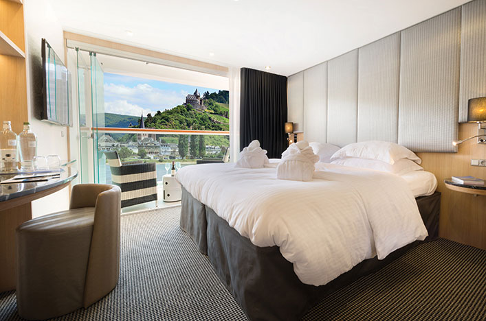 A Queen bed next to the Scenic Sun Lounge in the Standard Balcony Suite, with an open window showing the passing landscapes.