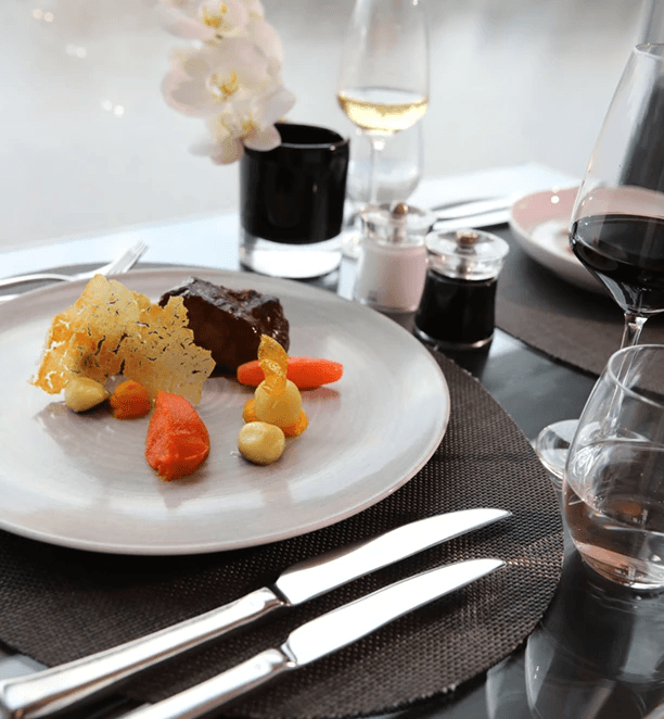 A plated meal of meat and vegetables paired with a glass of red wine in a Scenic suite