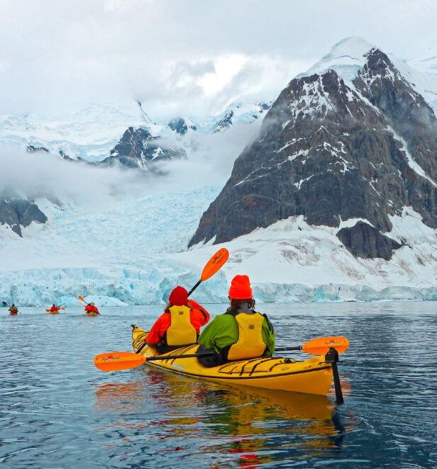 Kayakers paddling through icy Antarctic waters with snow-covered mountains in the background