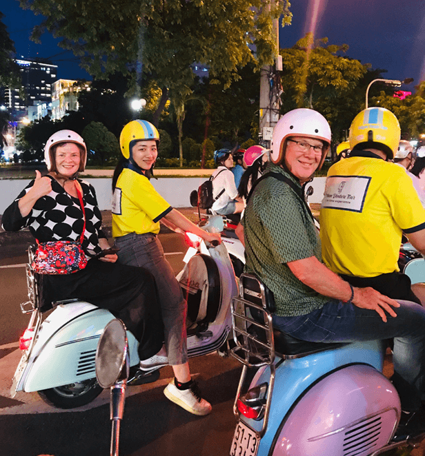 Tourists riding scooters with local guides during a Vietnamese street food tour at night.