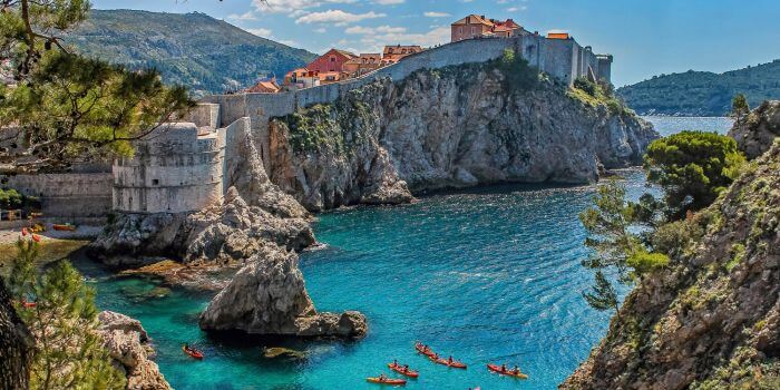 Kayakers paddling through crystal-clear waters beneath the historic stone walls of Dubrovnik, Croatia