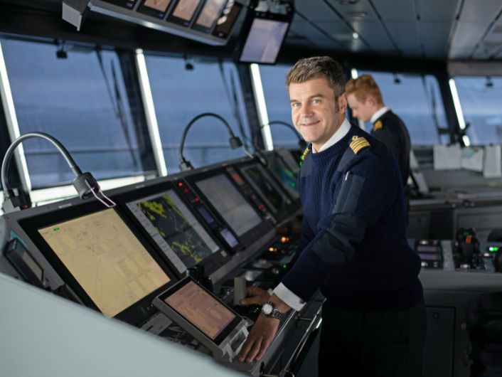 Ship captain at the Scenic Eclipse bridge surrounded by navigation monitors and controls