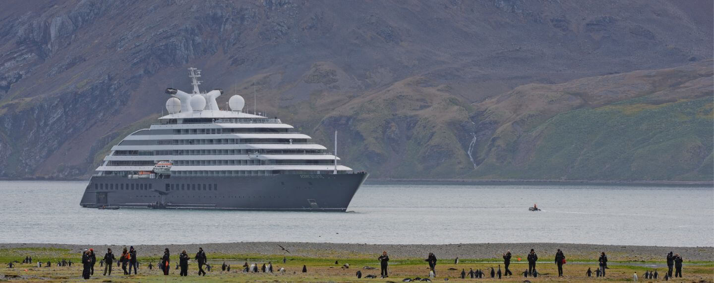 Scenic Eclipse anchored near Fortuna Bay in South Georgia with guests exploring the shoreline among penguins