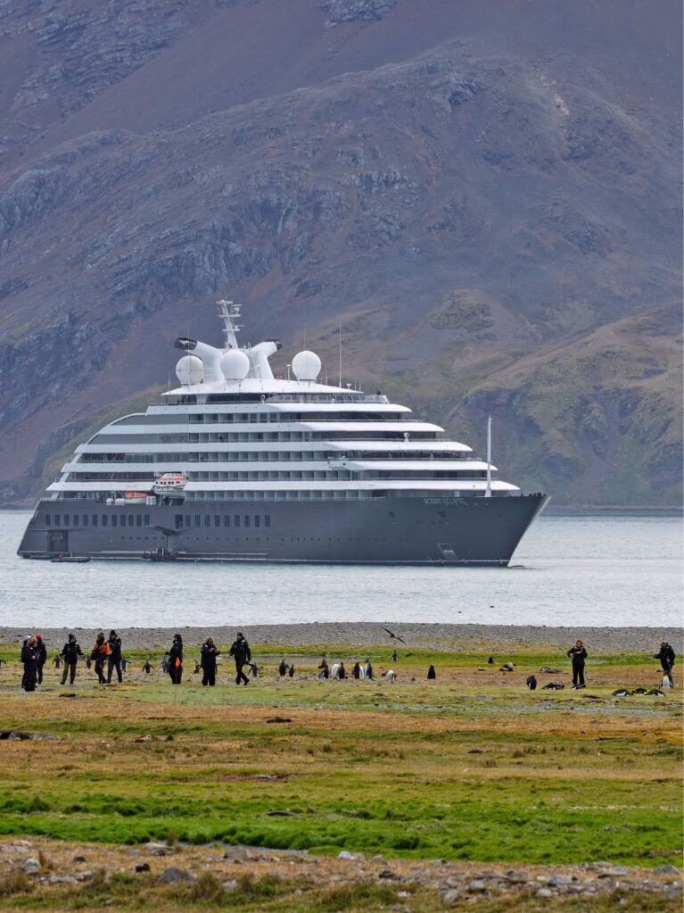 Scenic Eclipse anchored near Fortuna Bay in South Georgia with guests exploring the shoreline among penguins