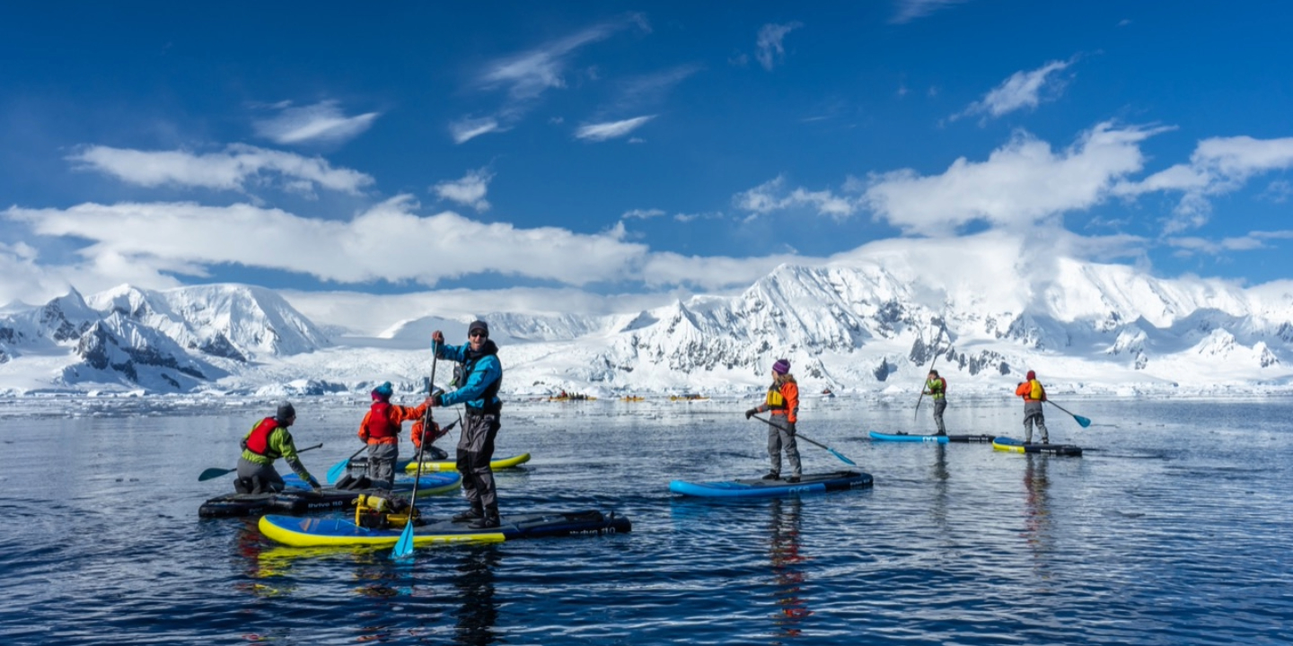 Group of paddle boarders on ocean in Antarctica with mountain behind